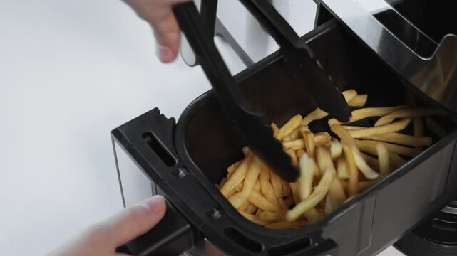 Woman stir fries with tongs in air fryer basket. Close-up with zoom