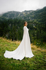 A radiant bride stands amid majestic mountains, her dress flowing softly in the mountain breeze. 