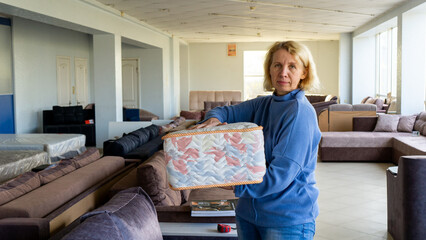 An adult female consultant with light hair is showing a mattress sample in a furniture store.
