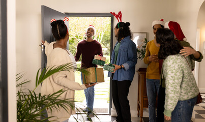 Welcoming guest at doorstep, multiracial friends celebrating christmas party, smiling together