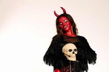 A beautiful woman embodies a devilish character, executing a captivating pose with a skull.