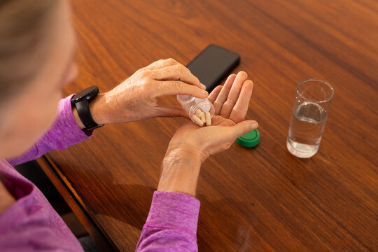 senior woman taking vitamins at home with smartphone and water on table