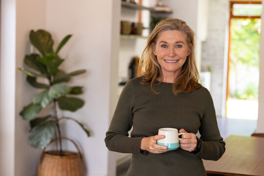 Smiling senior woman holding coffee mug at home, enjoying cozy morning