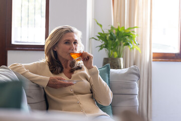 Relaxing at home, senior woman enjoying tea on cozy sofa