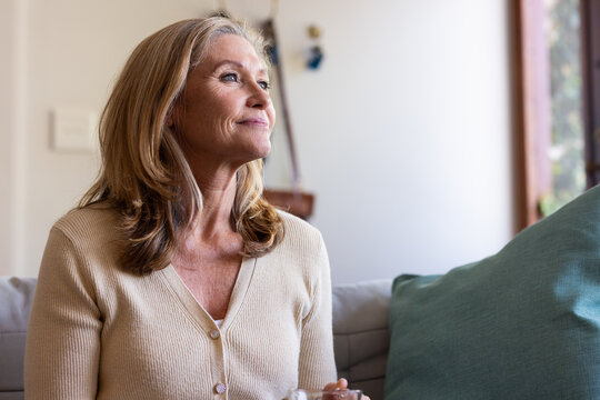 Smiling senior woman relaxing on sofa at home, enjoying peaceful moment