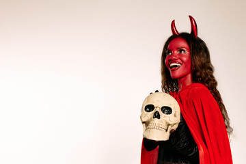 Dressed as a devil in a red cape, she joyfully poses with a skull, embracing the Halloween spirit.