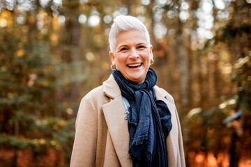 Mature woman in autumn forest, dressed in cozy fall attire, Reflection and connection with nature,...