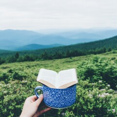 Obraz premium A serene landscape with a hand holding an open book in a blue mug.
