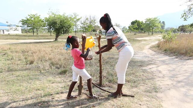 Young girl washing hands on gallon of water recycled and adapted on tree logs as hand washing stations also known as tippy taps