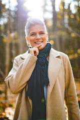 Mature woman in autumn forest, dressed in cozy fall attire, Reflection and connection with nature,...