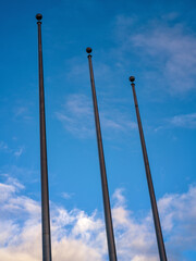 Three Empty Flag Poles Underneath Blue Sky and White Clouds.