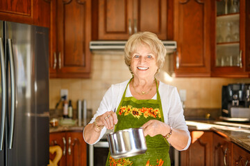 Naklejka premium Happy senior woman preparing lunch in modern kitchen cooking for the family at home