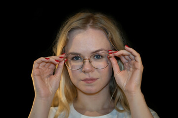 Young Woman Adjusting Glasses with Focused Expression on Black Background