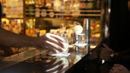 Smart bartender serving gin fizz or tonic with sliced lemon at luxurious bar, engaging lively conversation with VIP customer couple at side view in atmosphere at lighting warm nightclub. Vinosity.