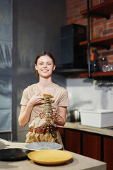 A woman preparing a fresh lobster dish in a stylish kitchen with a decorative plant in the background