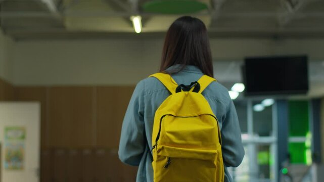 Back view from behind woman brunette girl student female girl walk go to classroom move to lesson education unrecognizable pupil with schoolbag walking in school corridor academy university college