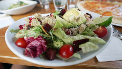 Close-up of a fresh and vibrant quinoa salad with mixed greens, avocado, cherry tomatoes, lime wedge, and beetroot on a dining table at a restaurant