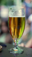 Cold glass of beer on a restaurant table, condensation visible on the outside, capturing a refreshing moment in an outdoor setting