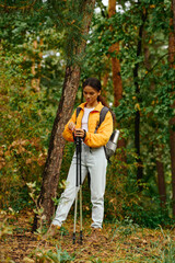 Amidst the colorful foliage, a young woman pauses with hiking poles, embracing nature beauty in...
