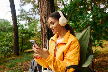 A young African American woman relaxes in the forest, wearing headphones and enjoying her music...