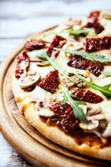 Pizza with mozzarella cheese, marinated tomatoes and fresh rocket. Wooden background. Close up.