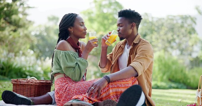Black couple, drinking and picnic with love on grass for romantic date, kiss and food basket of anniversary. Smile, people and fruit juice with affection, relationship bonding and commitment outdoor