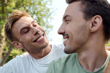 Fototapeta premium Two charming men share smiles and laughter while embracing in a vibrant park setting.