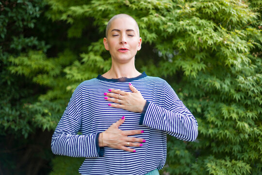Young female cancer patient meditating doing breathing exercises in her garden. Mental health, life balance, mindfulness and meditation concept.