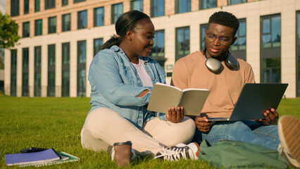 African American young male female students friends pupils sit at green grass in park studying...