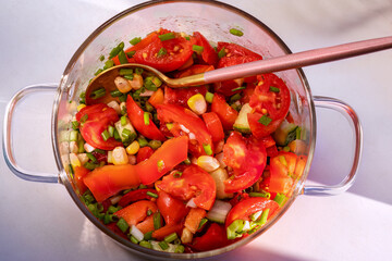 Tomato Salad. In glass saucepan. Top view, flat lay. Salad of tomatoes, bell peppers, cucumbers, sweet corn kernels, green onions