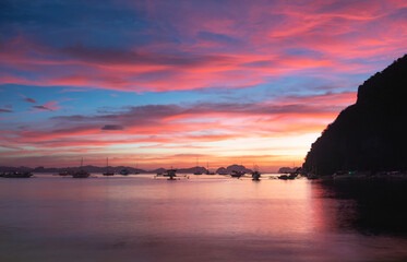 Sunset view over calm waters with boats anchored near the shoreline in a tropical location. El NIdo, Palawan.