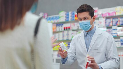 Female client choosing pills in pharmacy. Male pharmacist picking up medicine for woman. Man druggist wearing protective mask and communicating with client. Seller and buyer in drugstore.
