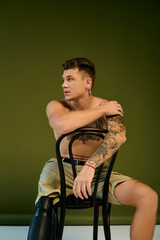 A young man with tattoos sits on a chair, showcasing his prosthetic leg in a vibrant studio...