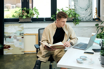 A young man with a prosthetic leg focuses on his work while seated at a stylish office desk.