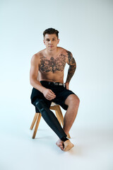 A tattooed young man poses on a stool in a studio, showcasing his prosthetic leg and body art.