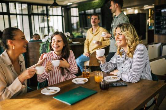 Group of female friends drinking coffee at the restaurant while the guys in the back try to flirt and send them drinks. Girl giggle and gossip about them.