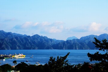 Przepiękna panorama na Palawan. Wysokie góry w tle, na pierwszym planie ocean i statki. Widok na góry, ocean i tropikalną naturę. Panorama na Coron na Filipinach. Turystyka na Filipinach. © Adam