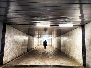 A lone person strolls through a narrow corridor illuminated by soft light, reflecting on smooth surfaces and creating a tranquil atmosphere