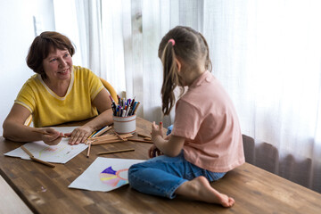 Grandmother and granddaughter happily create art together with colored pencils, enjoying their time