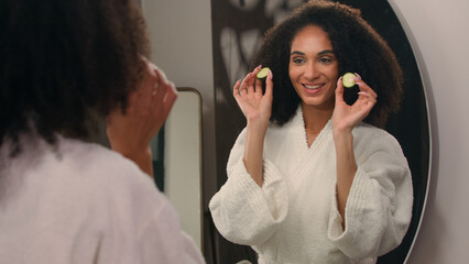 Happy African American woman funny girl in bathrobe having fun fooling around mirror reflection...