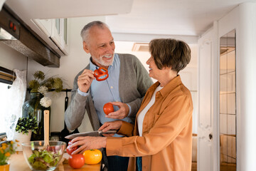 Positive senior old elderly couple spouses husband and wife cooking together, preparing food meal