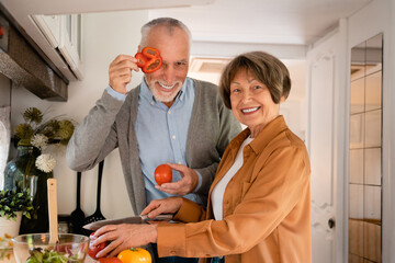 Funny old elderly senior couple spouses cooking, cutting vegetables at home kitchen, preparing food