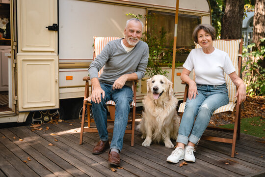 European senior couple relaxing on the beach chairs with dog traveling on holidays