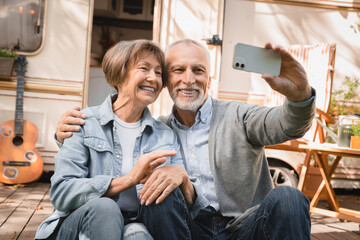 Fototapeta premium Senior grandparents having videocall conversation online on cellphone while traveling by trailer