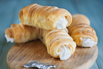 Stack of flaky puff pastry cream horns, Cannoncini, filled with vanilla cream on rustic table.  Selective focus with blurred background.