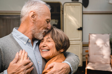 Portrait of happy smiling senior couple grandparents hugging during travel trip voyage by trailer