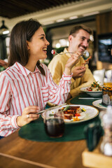Group of happy friends eating lunch together in a restaurant. They eat delicious salads,...