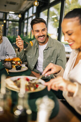 Group of happy friends eating lunch together in a restaurant. They eat delicious salads, hamburgers, bread and meat.