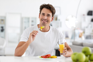Good looking healthy man has breakfast at a table indoors.