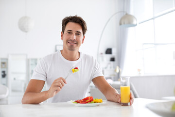 Good looking healthy man has breakfast at a table indoors.
